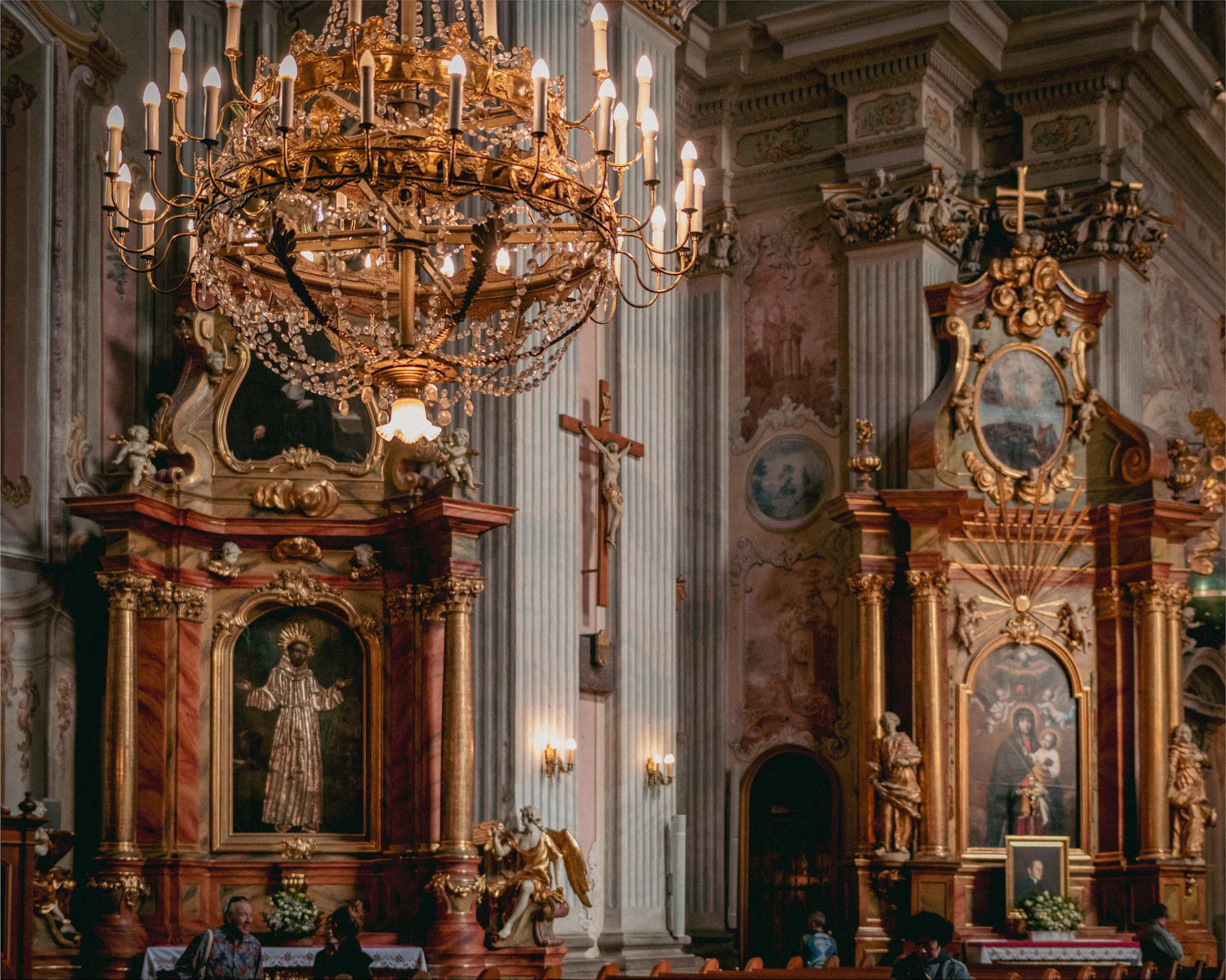 A chandelier and gilded altar surrounded by richly decorated columns in a Polish church.