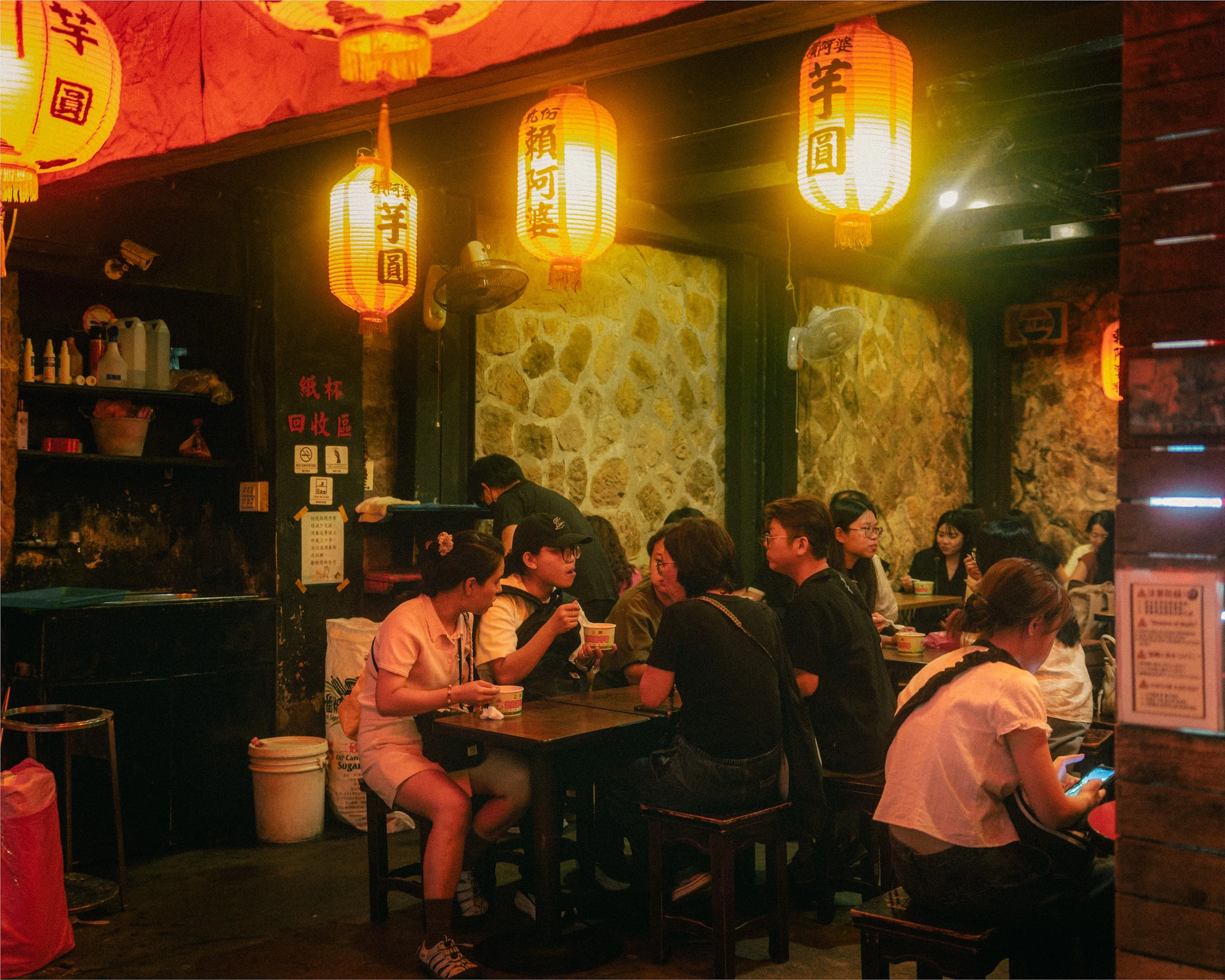 People seated outside a small Taiwanese restaurant beneath glowing lanterns at night.